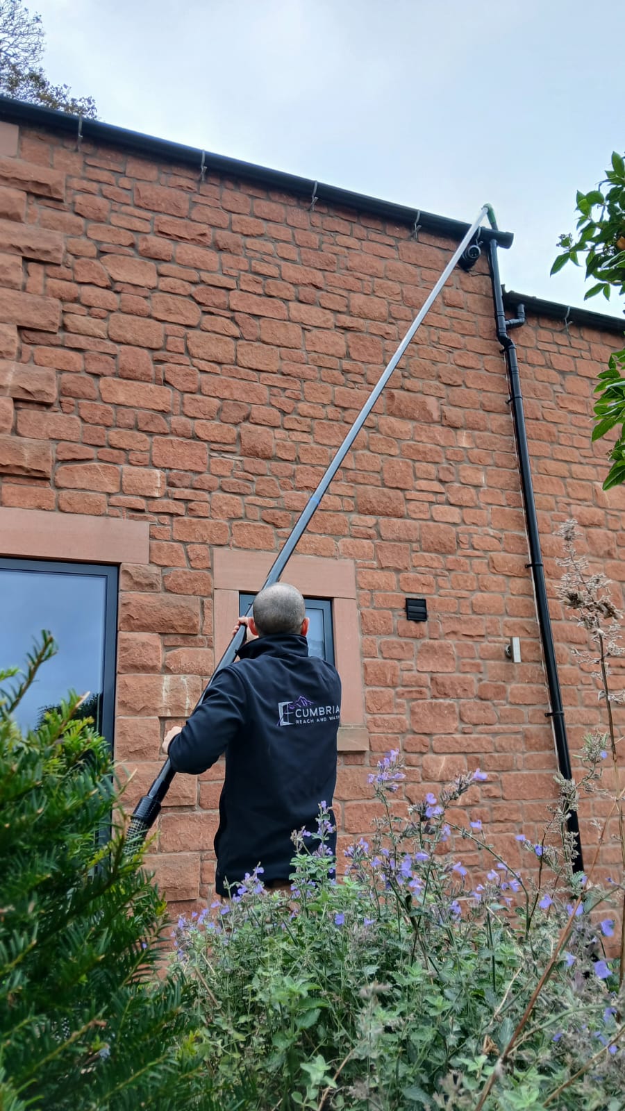 One of the team cleaning windows on a red sandstone building with a water-fed pole