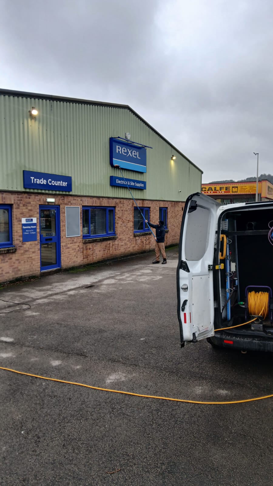 Cleaning the windows of a trade counter unit, with the van and hose reel in the foreground